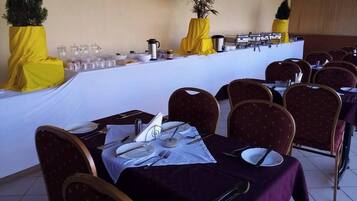 Un salón de conferencias con mesas dispuestas para una reunión, equipado con tarjetas de identificación, platos, cubiertos y una estación de café.