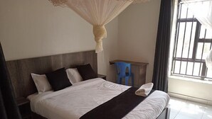 Hotelkamer met een groot bed, een houten hoofdeinde, een klein bureau en een raam met tralies.
