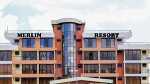 Een gebouw met twee delen, voorzien van de aanduidingen 'MERLIN' en 'RESORT'.