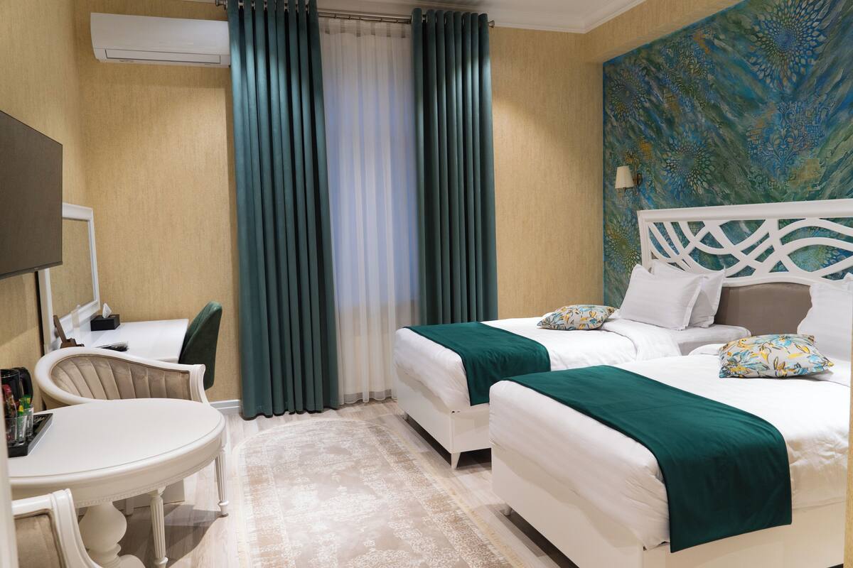 A hotel room with two beds, a desk, a chair, and a TV.