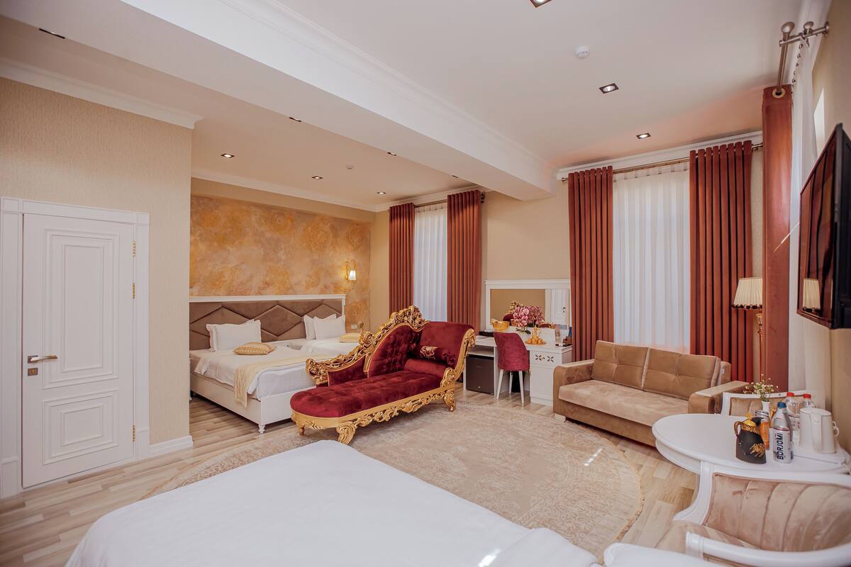 A hotel room with a large bed, a red sofa, a desk with a computer, and a TV mounted on the wall.