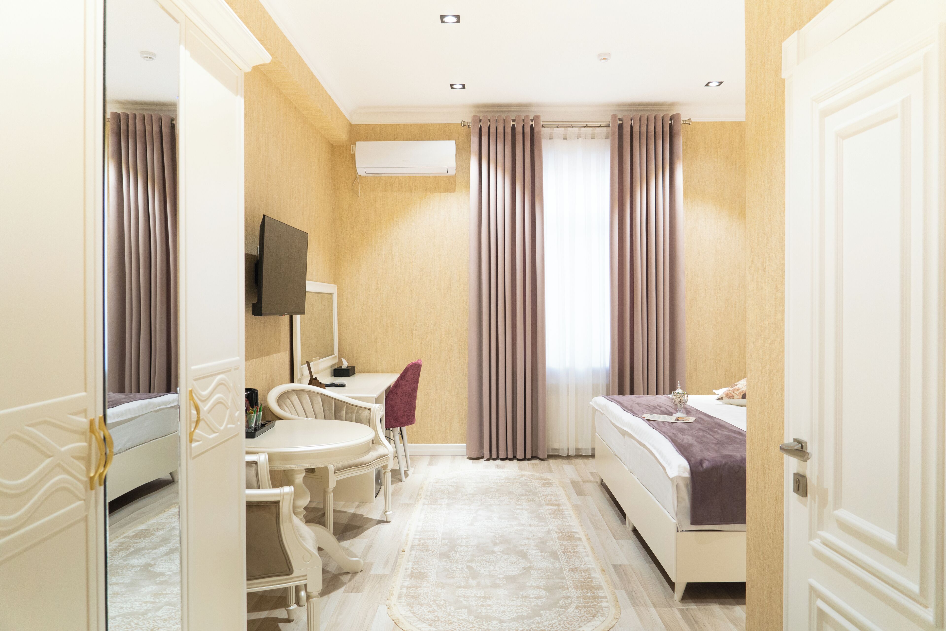 Habitación de hotel con cama, escritorio con silla, televisor y ventana con cortinas.
