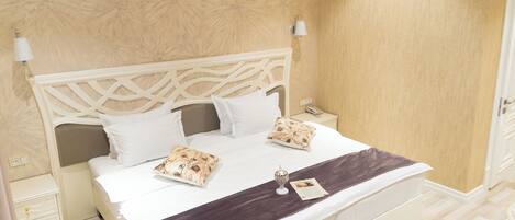 A neatly made bed with white linens and decorative pillows, a bedside table with a lamp, and a wall with a floral pattern.