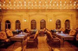 A dining area with wicker chairs and tables, brick walls, and string lights.