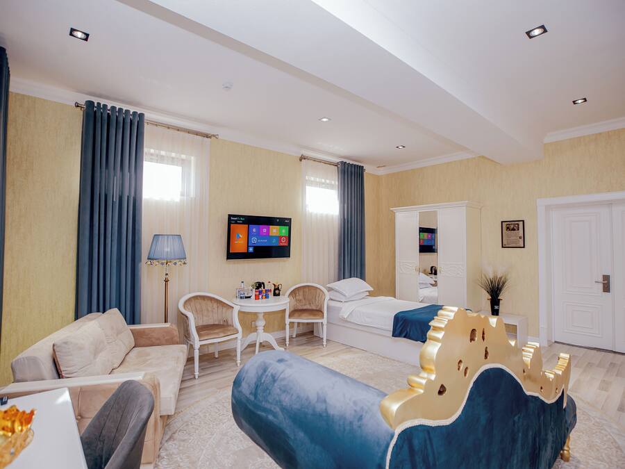 A hotel room with a sofa, a bed with a decorative headboard, a television, a small table with chairs, and a white door.
