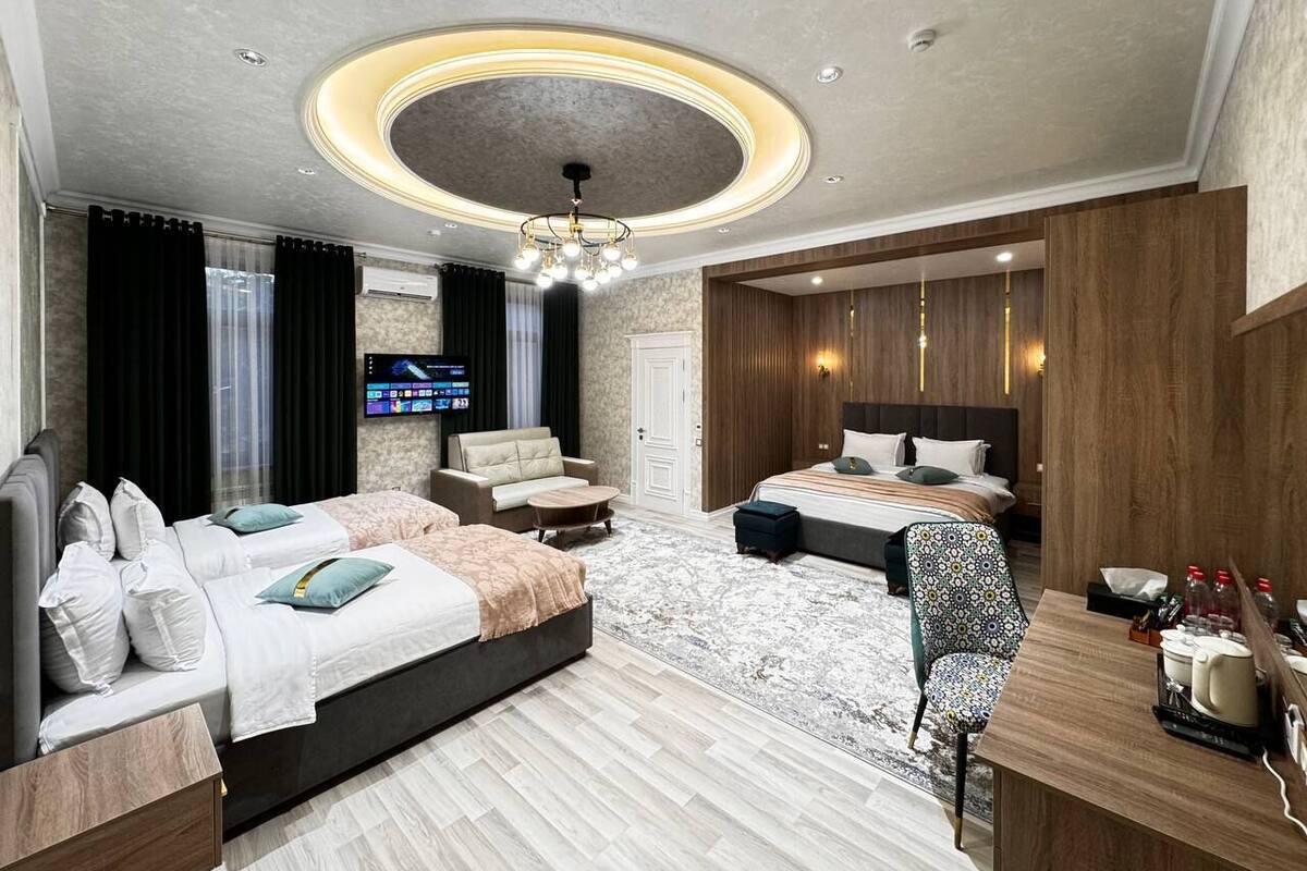 A modern hotel room with a large bed, a smaller bed, a sofa, a desk, and a TV.
