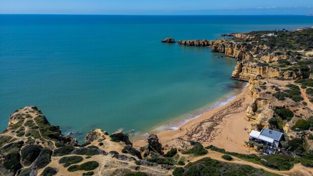 Un paisaje costero con una playa, acantilados rocosos y un edificio de techo plano.