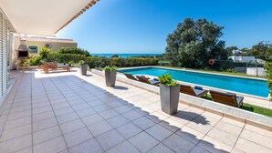 Un amplio espacio al aire libre con piscina, sillas de descanso y una parrilla.