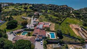 Vista aérea de una propiedad costera con varias construcciones, una piscina y vista al mar.