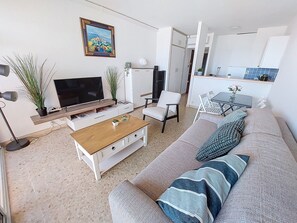 Een moderne woonkamer met een bank, salontafel, televisie en een eethoek met stoelen en een tafel.