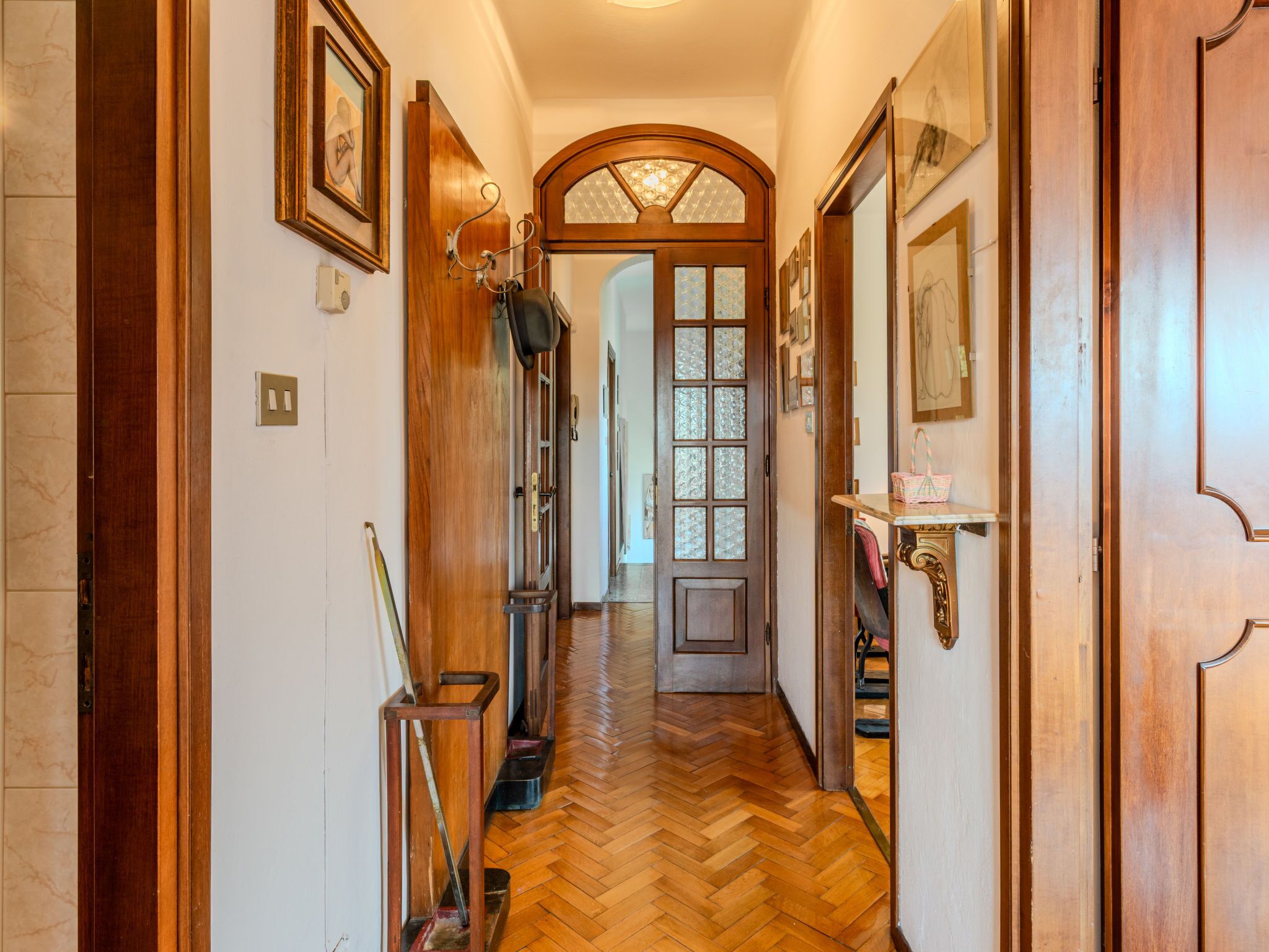 Um corredor com portas de madeira, piso em padrão herringbone e quadros nas paredes.