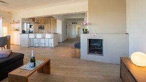 A modern living room with a fireplace, a kitchen in the background, and a bar area with stools.
