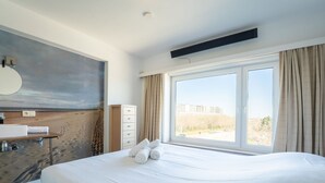 A hotel room with a large bed, a bathroom with a sink and mirror, and a view of the beach through the window.