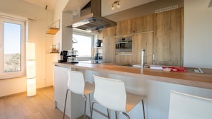 A modern kitchen with a wooden backsplash, stainless steel appliances, and a bar area with white chairs.