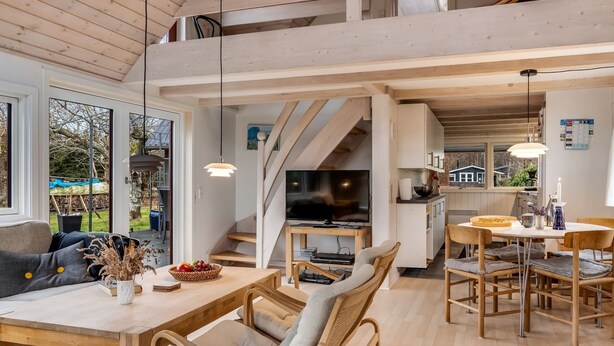 Un vaste espace de vie doté d’un haut plafond, de poutres en bois, d’une table à manger avec des chaises, d’un téléviseur et d’un coin cuisine avec une cuisinière.