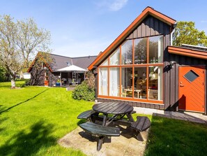 Ein modernes Haus mit großem Panoramafenster, einer Holzterrasse und einem Picknicktisch.