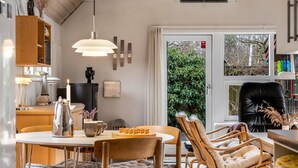 Une cuisine moderne avec un coin repas, des meubles en bois, des luminaires suspendus et une vue à travers une porte vitrée.
