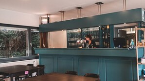 Een bar met een blauwgroene bar, barkrukken en een uitzicht op het buitengebied door een groot raam.