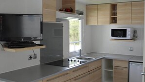 Een moderne keuken met een inbouwfornuis, magnetron en een flatscreen televisie op een houten plank.
