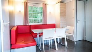 Een kleine kamer met een rode bank, witte stoelen, een tafeltje, een raam met gordijnen en een deur.