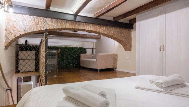A bedroom with a bed, two white towels, a chair, a wooden bench, a green wall, and a white door.