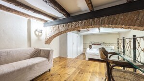 A cozy room with a wooden floor, a white sofa, a glass table, and a bed with white bedding.