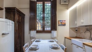 A dining area with a table set for four, a window with shutters, and a kitchen with white cabinets and a sink.