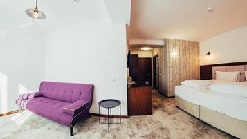 Habitación de hotel con un sofá morado, una mesita redonda pequeña, una cama y un escritorio de madera.