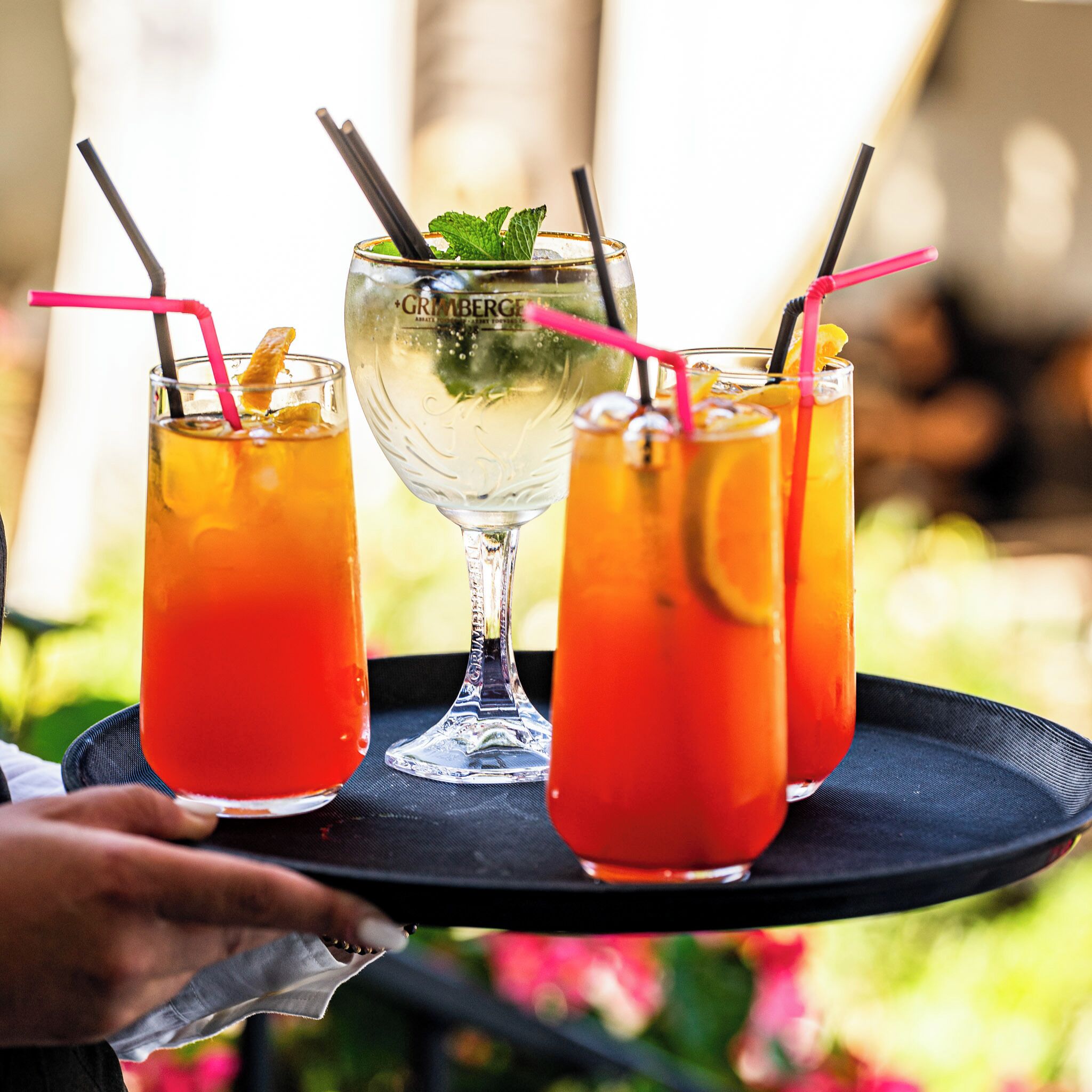 Three glasses of a red beverage on a tray, with a clear glass in the center.