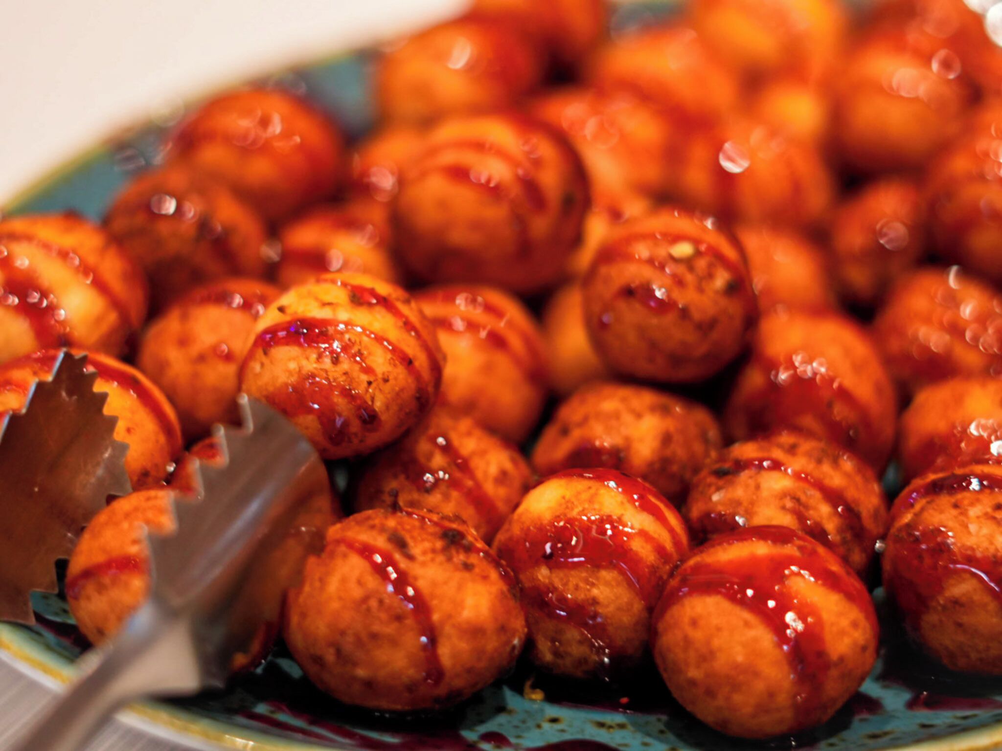 A plate of round, golden-brown food items with a glossy, reddish sauce, likely a type of fried snack or appetizer.