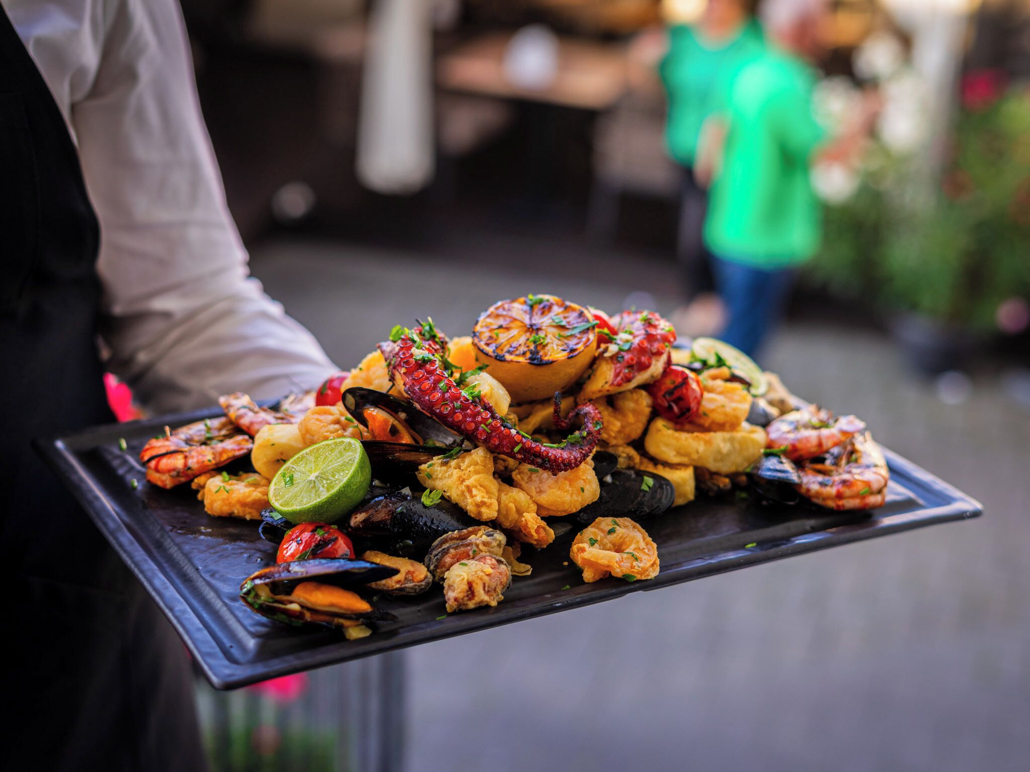 A tray of seafood including mussels, shrimp, and squid, garnished with herbs and a lime wedge.