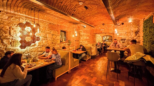 A restaurant with stone walls and wooden flooring, featuring hexagonal light fixtures and patrons dining. - Hotel Bucheland (Gura Humorului)