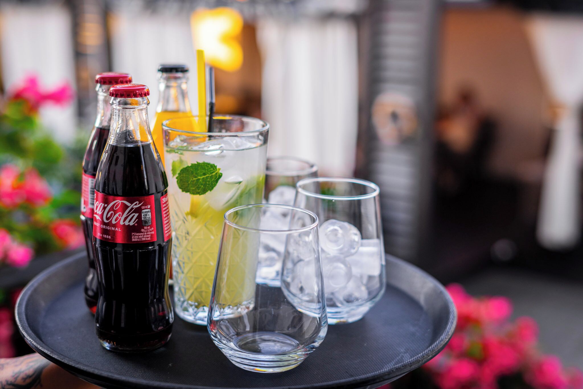 A tray with a Coca-Cola bottle, a glass with a yellow drink and mint, and two empty glasses with ice.