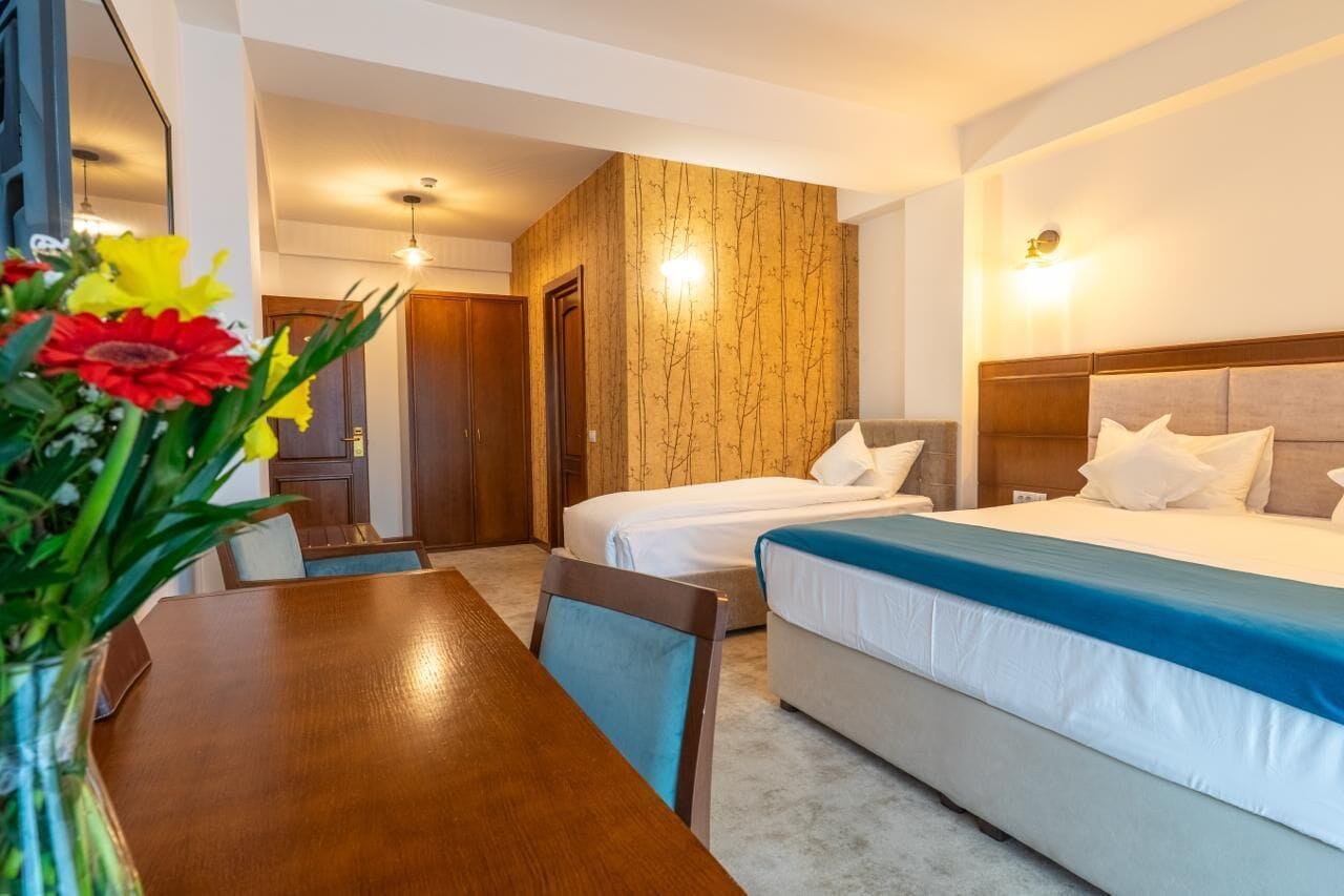 Une chambre d’hôtel avec deux lits, un mur décoratif en bois, une table à manger avec des chaises et un vase de fleurs.