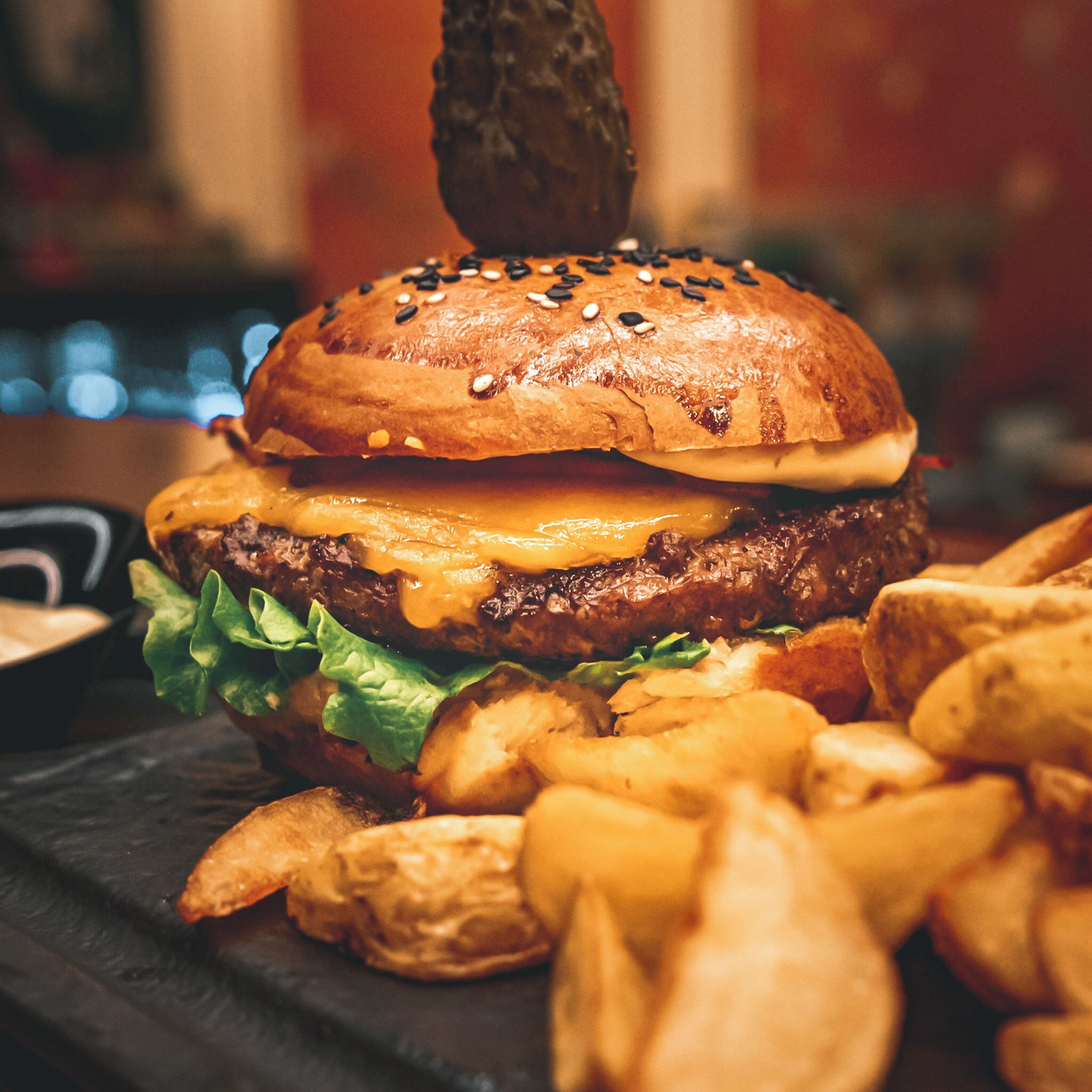 En hamburgare med ett sesamfröbröd, ost, sallad och en köttfärsbiff, serverad med pommes frites.
