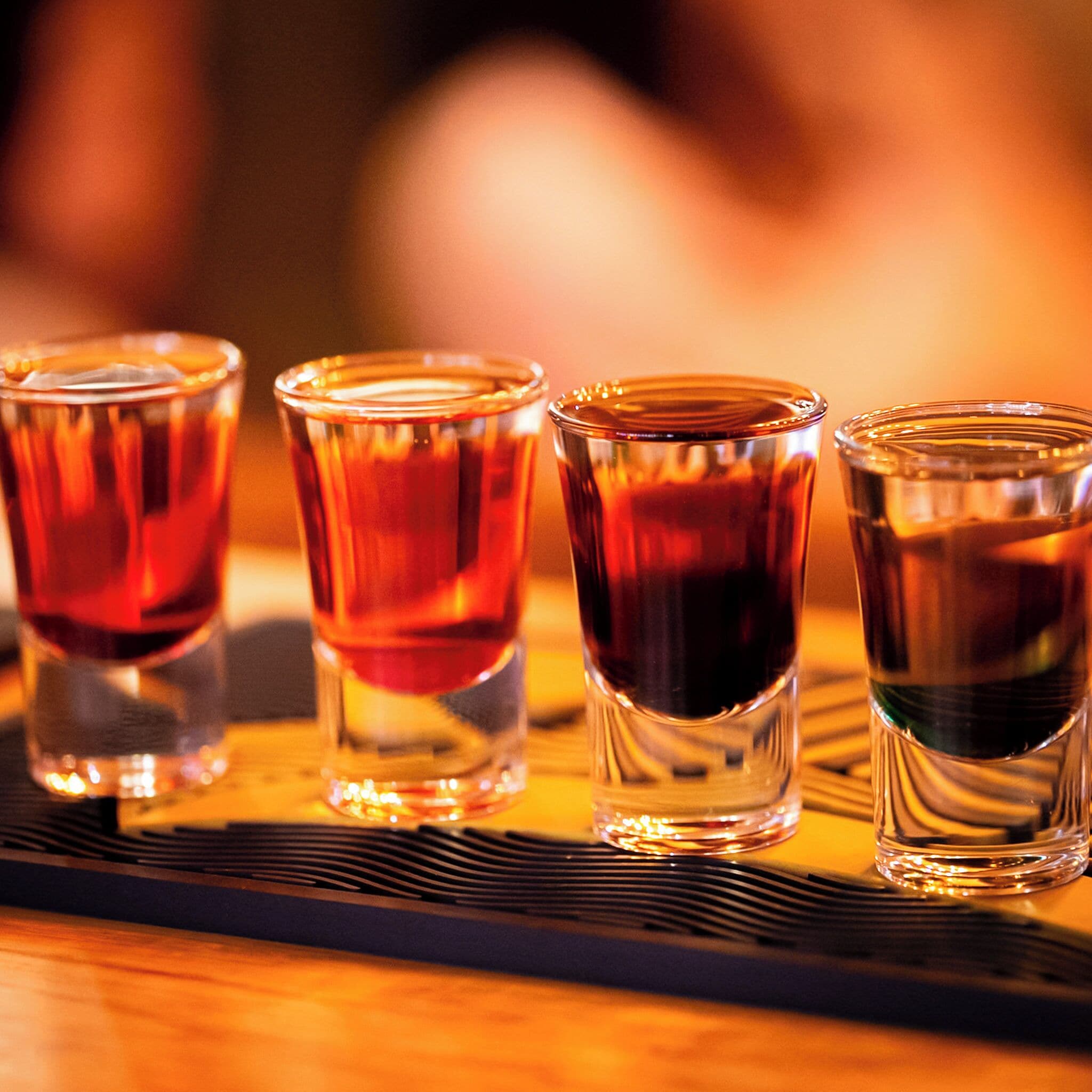 Vier shotglazen gevuld met een donkere vloeistof, gerangschikt op een zwarte schaal.
