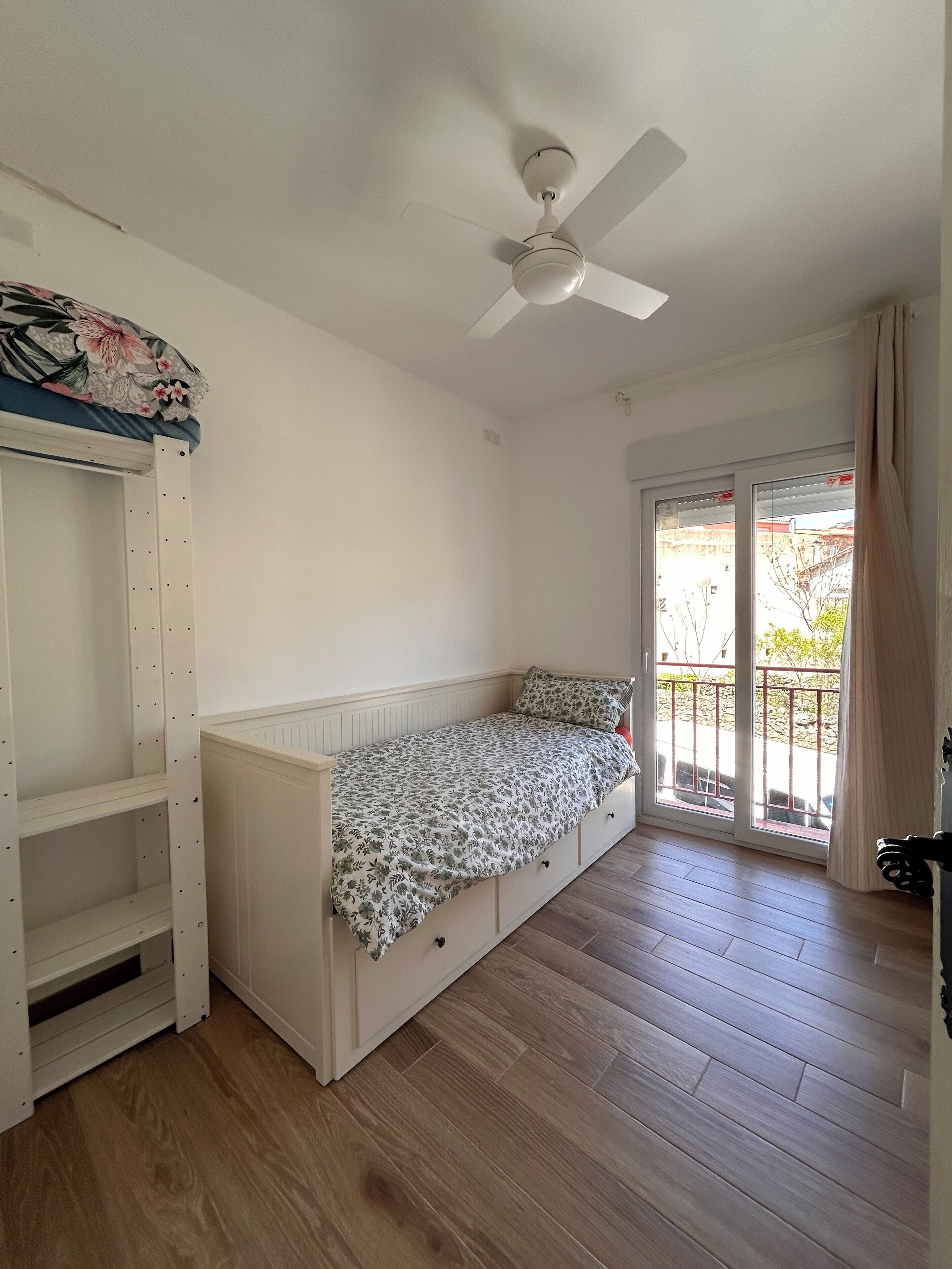 Une chambre à coucher avec un lit, un ventilateur de plafond, une fenêtre donnant sur un beau paysage et un plancher en bois.