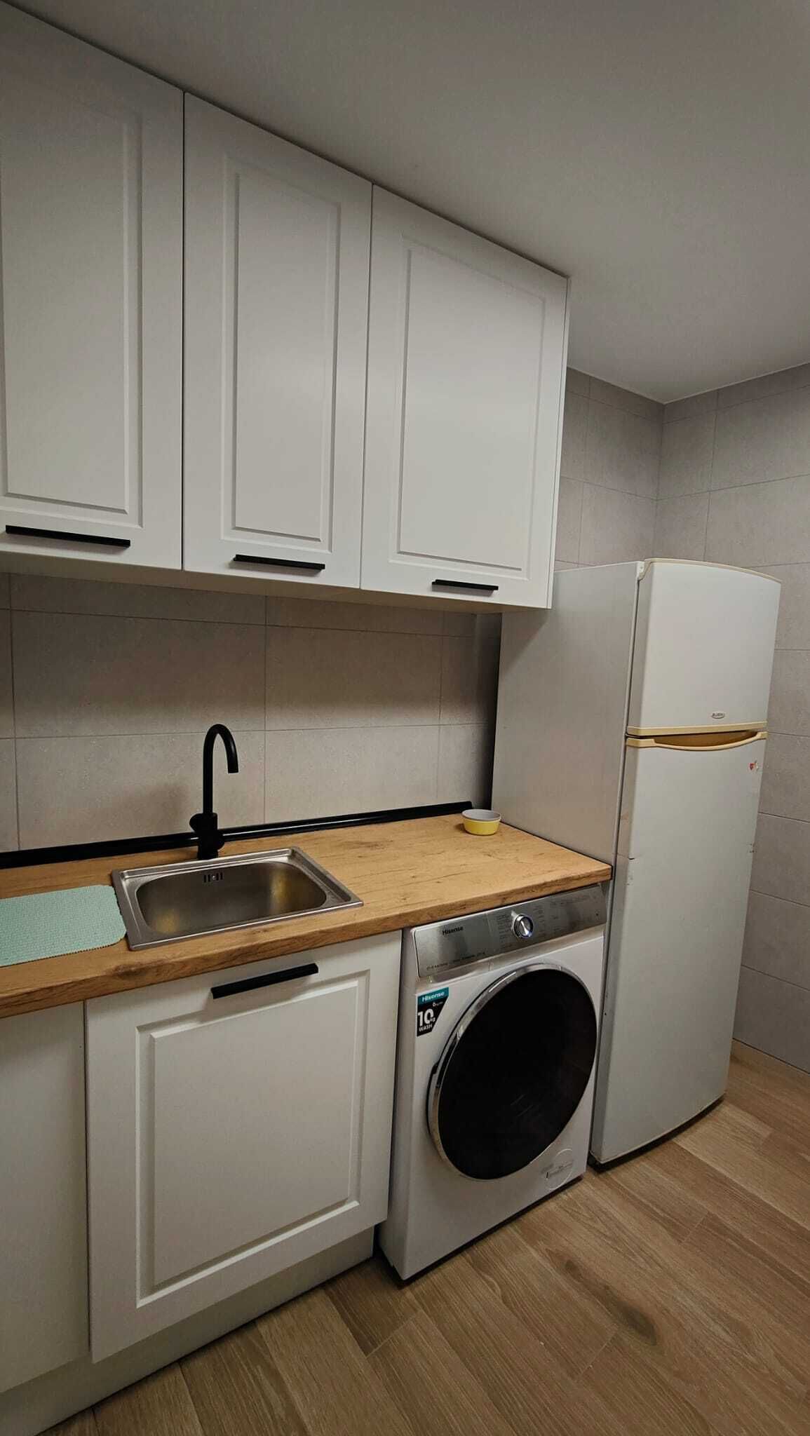 Une cuisine compacte avec des meubles blancs, un évier en acier inoxydable, un lave-linge et un réfrigérateur.