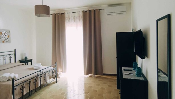 Habitación de hotel con cama, televisión, una mesita con lámpara y ventana con cortinas.