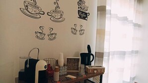 Una habitación acogedora con un aparador de madera, un adhesivo mural con temática de café y una ventana con cortinas de gasa.