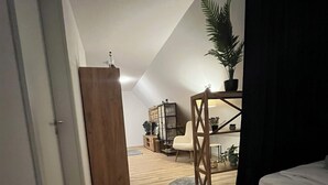 Une chambre avec un lit en bois, un petit tapis rond, une chaise en bois, un bureau et une plante en pot.