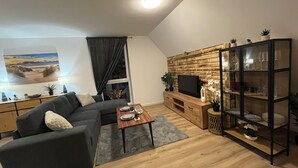 Un salon moderne avec un canapé d’angle, une table basse en bois, un téléviseur posé sur un meuble en bois et une vitrine en verre.