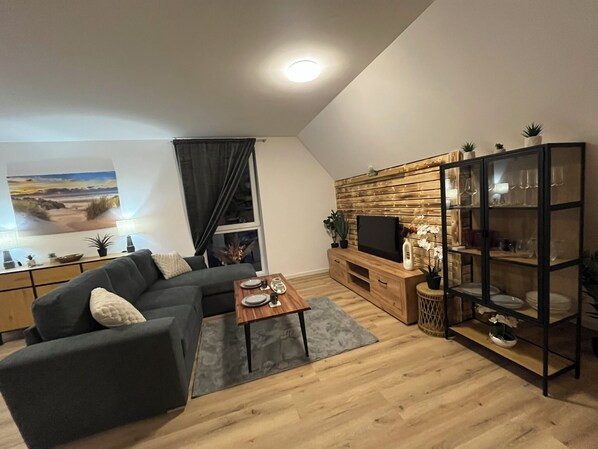 Een moderne woonkamer met een modulaire bank, een houten salontafel, een tv op een houten dressoir en een glazen vitrinekast.