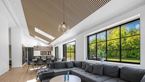 Una sala moderna con un amplio sofá seccional, una mesa redonda de centro y vistas a un jardín exuberante a través de ventanas de piso a techo.