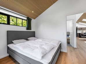 A modern bedroom with a large bed, a wooden ceiling, and a view of the outdoors through a window. - "Tähti" - 425m from the sea by Interhome (Føllenslev)