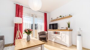 Ein modernes Wohnzimmer mit einem Holztisch, einem grauen Sessel, einer weißen Schrank mit Fernseher und einem roten Vorhang.