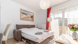 Ein Schlafzimmer mit einem Bett, einem Sessel, einem Tisch mit einer Vase, einer Lampe und einem Fenster mit Vorhängen.