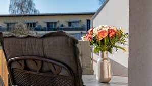 Ein Balkon mit einem Stuhl und einer Tischvase mit Blumen.