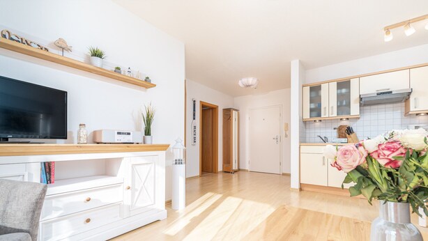 Eine moderne Küche mit weißen Schränken, einer Holz Arbeitsplatte und einem Fernseher. Auf dem Boden steht ein Blumenvasen.