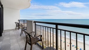 A balcony with a view of the beach, featuring two chairs and a table.
